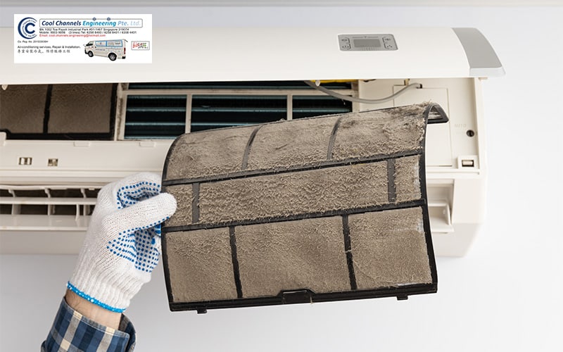 Gloved hand holding a dusty aircon filter removed from an open unit.